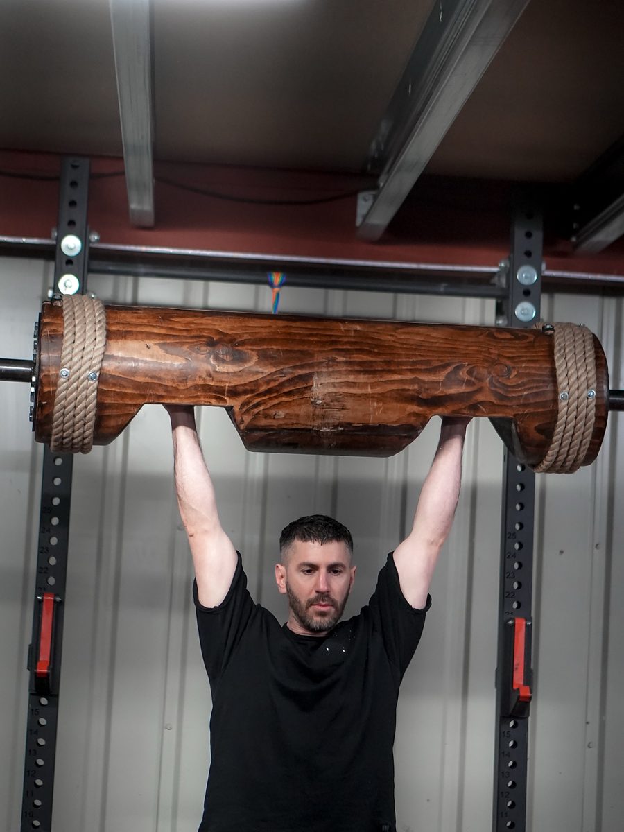 Alexandros pressing a strongman log overhead in the gym